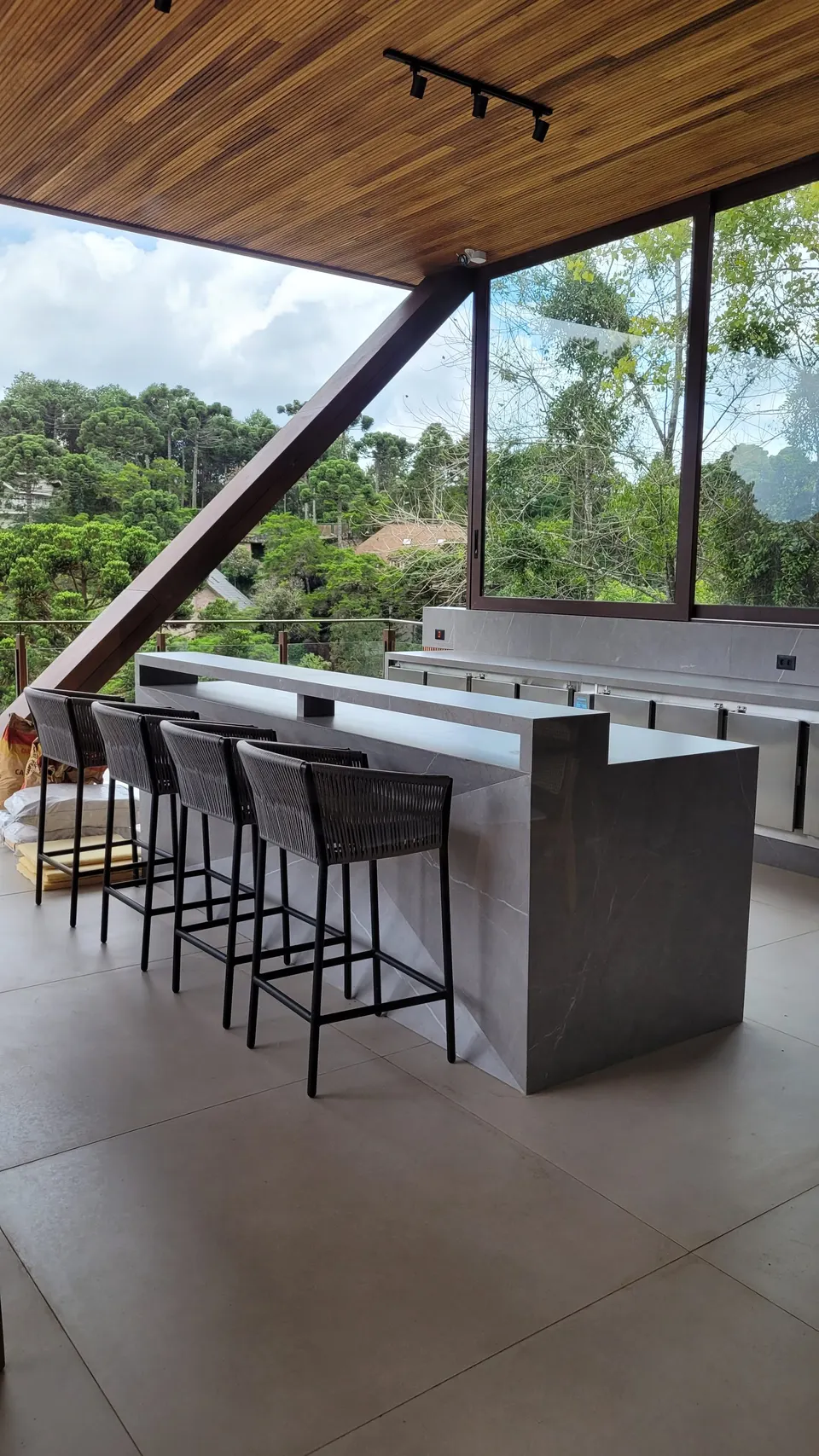 Ilha na área gourmet/outdoor em lâmina cinza, com frente preta e vista externa de montanhas ao fundo
