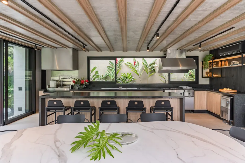 Tampo de mesa em lâmina branca com veios cinzas, em ambiente de área gourmet com bancada de fundo em tom escuro e teto com estrutura de madeira — Lâmina ultracompacta Branco