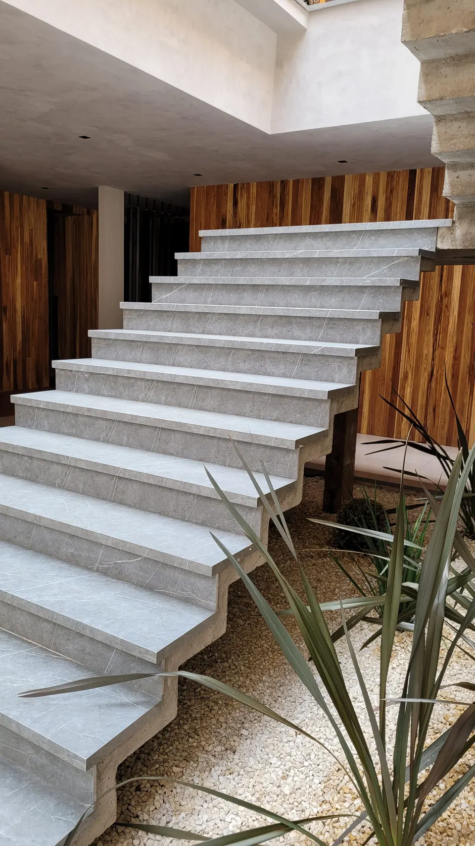 Escada interna em lâmina de pedra cinza, com degraus uniformes e acabamento polido, integrada a ambiente moderno com revestimento de madeira nas laterais