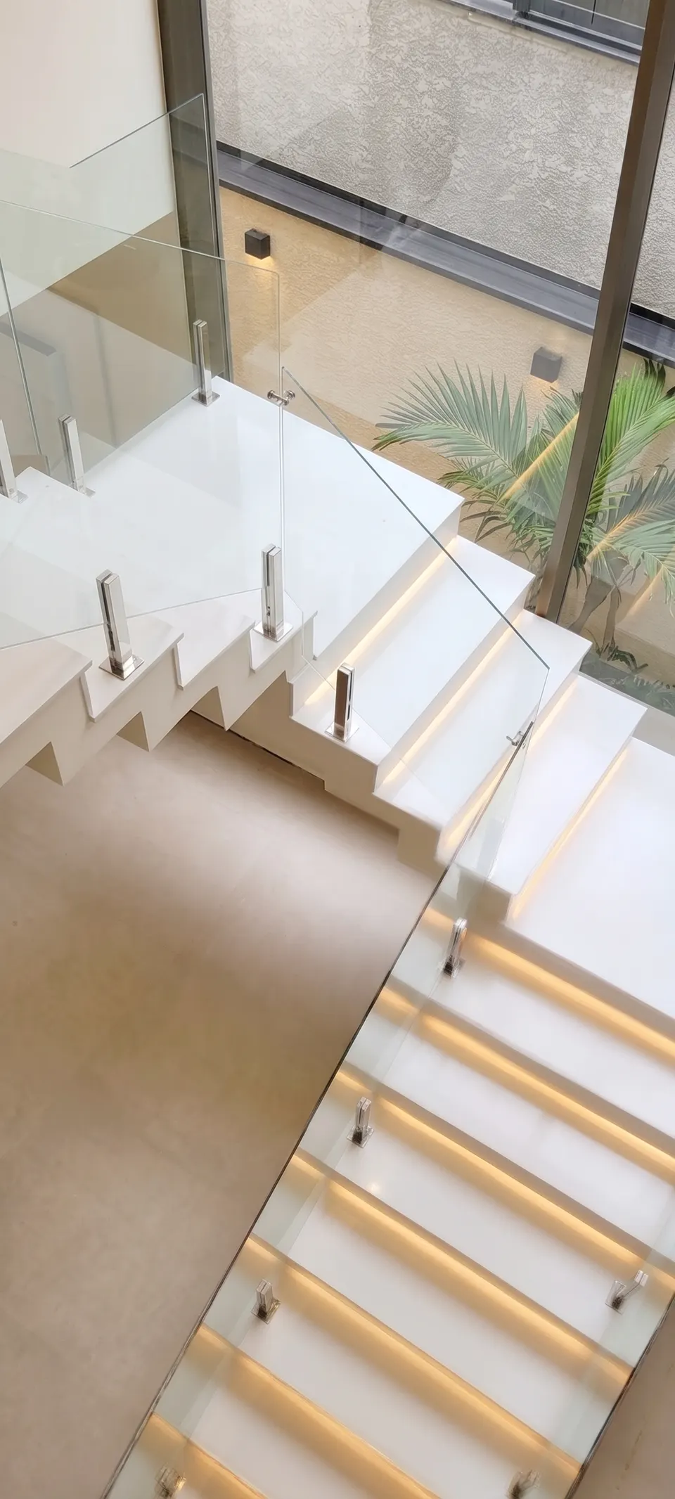 Escada em quartzo branco com degraus em balanço, iluminação de led embutida sob cada pisada e guarda-corpo de vidro