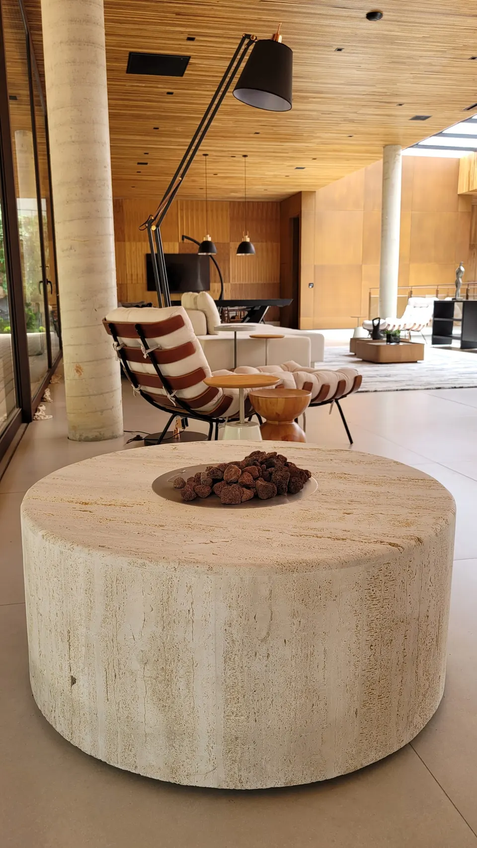 Mesa redonda em mármore travertino com acabamento natural e fogo central, instalada em área gourmet externa — Mármore Travertino Romano